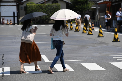 Two young japanese woman with umbrellas walking over a zebra crossing in Kyoto-Japan.