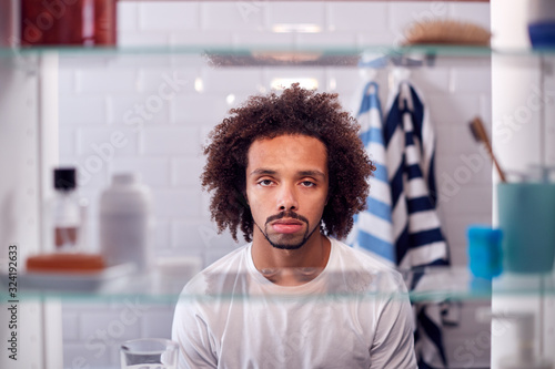 View Through Bathroom Cabinet Of Unhappy Young Man Getting Ready For Work photo