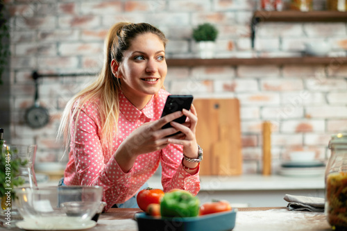 Beautiful woman in kitchen. Young woman writing message on phone. 
