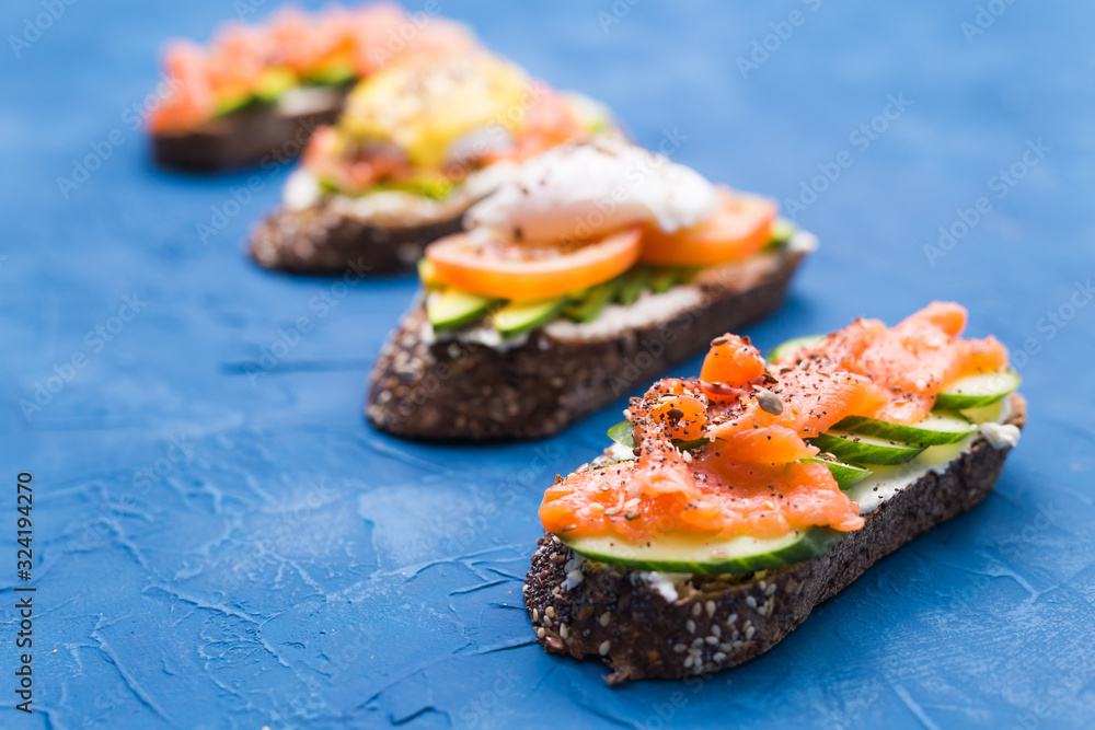 Sandwiches with smoked salmon, eggs, sauce and avocado on blue background. Concept of breakfast and healthy nutrition. Sandwiches with smoked salmon, eggs, sauce and avocado on blue background. Concept of breakfast and healthy nutrition.