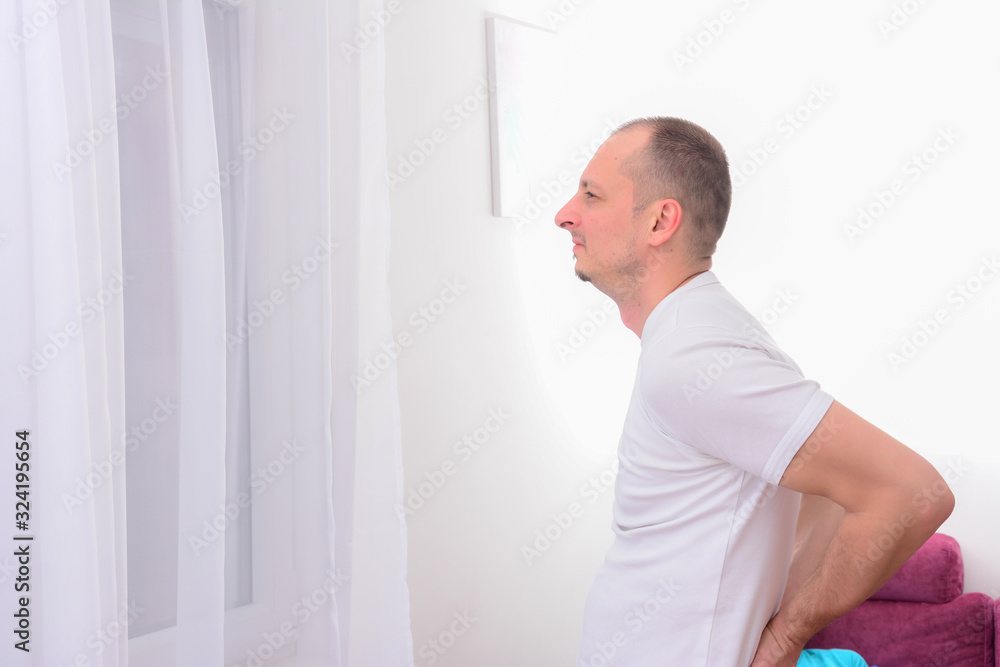 Side view of unhappy man suffering from backache at home. Male feeling sharp lower back pain indoor, health and problems, medicine Side view of unhappy man suffering from backache at home. Male feeling sharp lower back pain indoor, health and problems, medicine