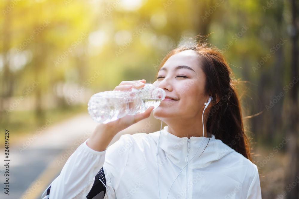 Closeup image of an asian female runner drinking water from bottle after jogging in city park Closeup image of an asian female runner drinking water from bottle after jogging in city park