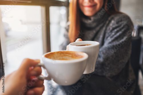 Closeup image of a woman and a man clinking coffee mugs in cafe photo