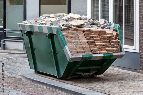 Neat industrial skip parked on the clean sidewalk full loaded with bricks and rubble in Dordrecht in the Netherlands