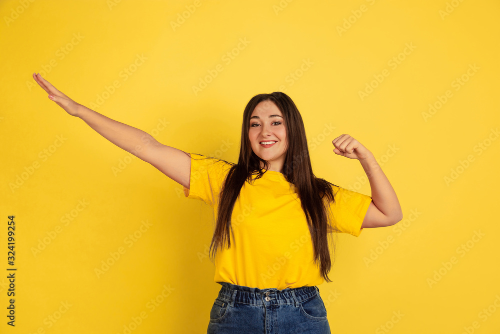 Winner gesture. Caucasian woman's portrait isolated on yellow studio background. Beautiful female brunette model in casual style. Concept of human emotions, facial expression, sales, ad, copyspace. Winner gesture. Caucasian woman's portrait isolated on yellow studio background. Beautiful female brunette model in casual style. Concept of human emotions, facial expression, sales, ad, copyspace.