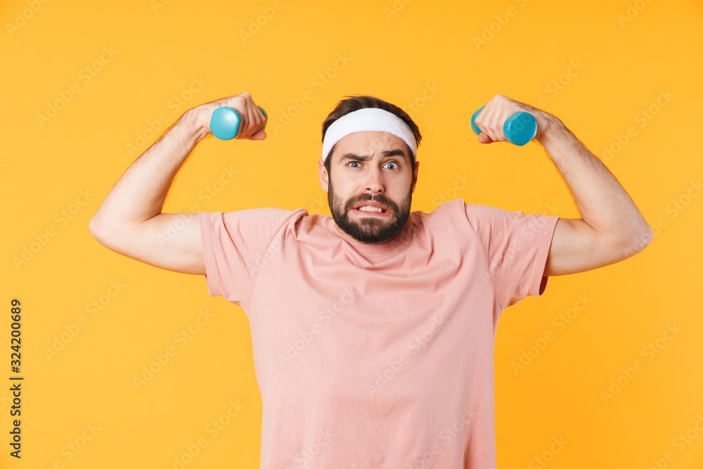 Fototapeta premium Image of muscular athletic young man having fun and lifting dumbbells