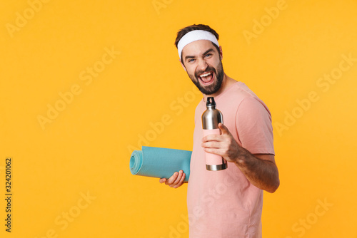 Image of athletic young man carrying fitness mat and water bottle