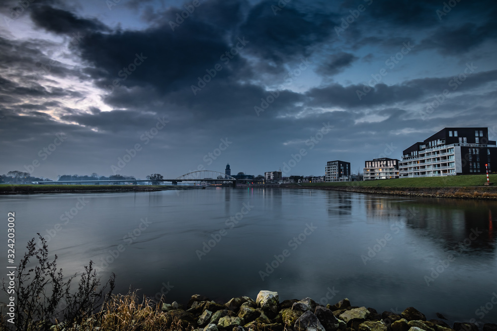 Fototapeta premium The Deventer skyline along a river during a cloudy sunset with apartment on the side in the Netherlands