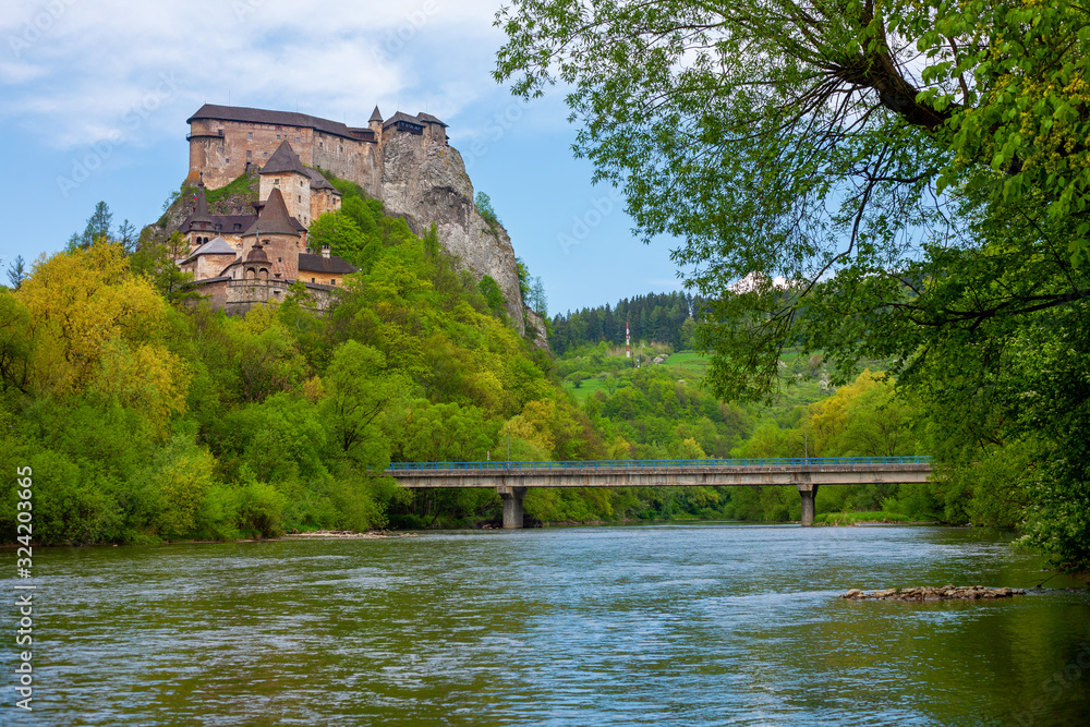 Fototapeta premium The picturesque Orava castle on top of a cliff with autumn forest and river with bridge in the foreground in Slovakia