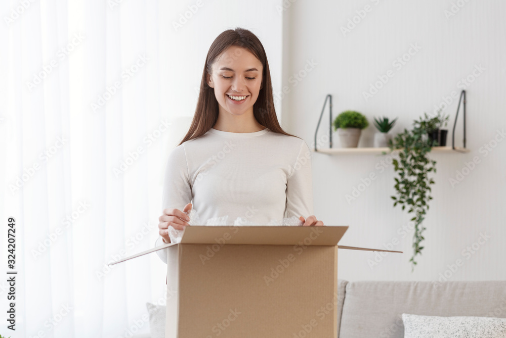 Happy millennial girl at home open cardboard delivery Happy millennial girl at home open cardboard delivery