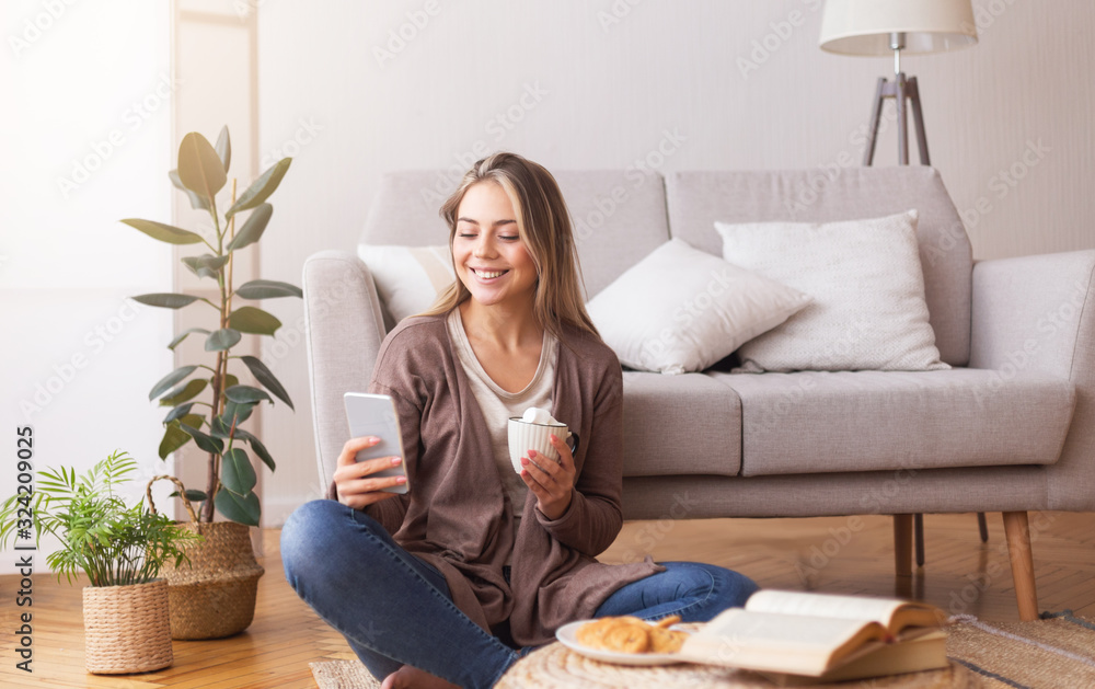 Cheerful woman with cellphone enjoying coffee on floor Cheerful woman with cellphone enjoying coffee on floor