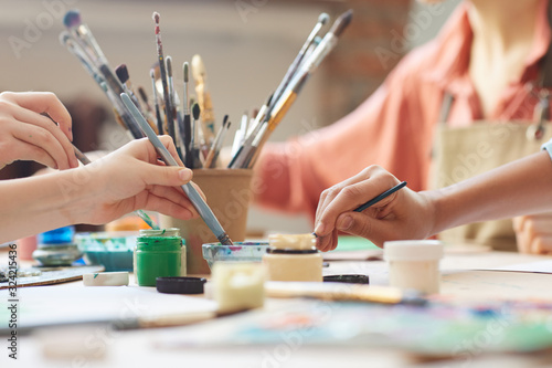 Fototapeta Naklejka Na Ścianę i Meble -  Close-up of children using paintbrush and watercolor paints to paint a pictures at the table