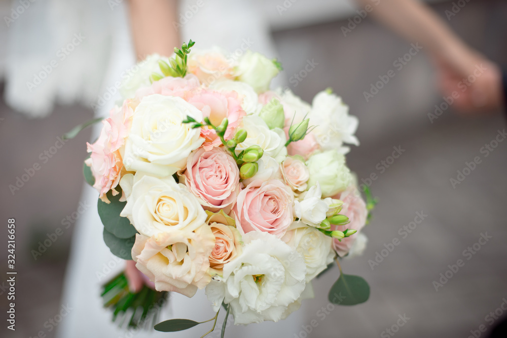 Close-up groom in a suit and the bride in a white dress are standing and holding a bouquet of peach roses, eustomas and flowers and greenery. Close-up groom in a suit and the bride in a white dress are standing and holding a bouquet of peach roses, eustomas and flowers and greenery.