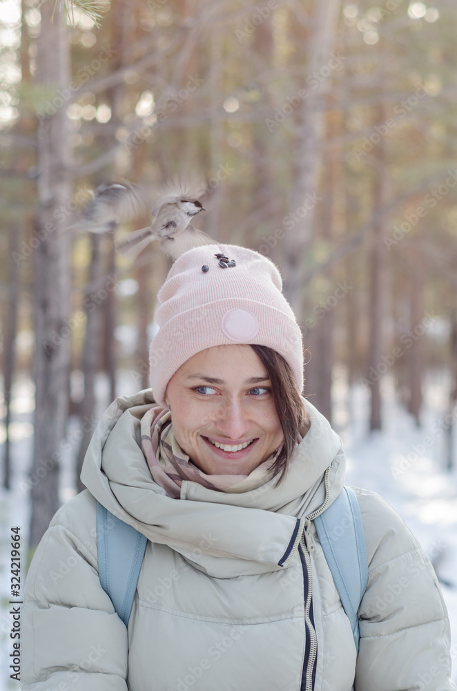 Obraz premium girl in winter clothes smiles and feeds the birds from the head in the park