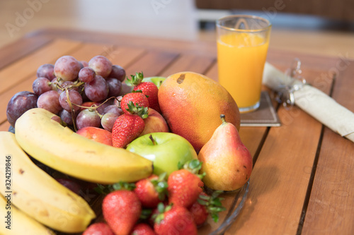 Fruits (bananas, apples, mango, grapes, strawberries) placed on a table next to a glass of orange juice ready for breakfast