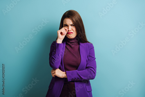 offended girl crying and wiping tears with hand while standing on blue background