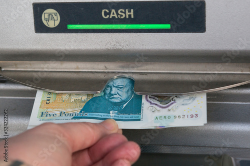 Person withdrawing money from UK United Kingdom cash machine ATM withdrawal hand holding five pound note. British economy visiting England British Tourism concept idea