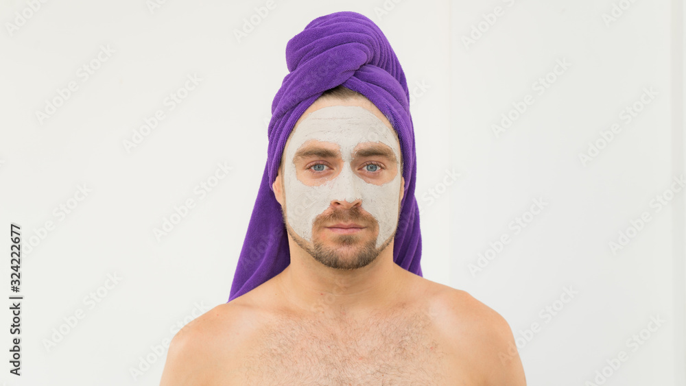 Funny handsome young man with purple towel on his head and face cosmetic mask after bath .Man wears facial clay mask enjoys beauty tratments.Funny content for Womens Day, spa or Valentine day. Funny handsome young man with purple towel on his head and face cosmetic mask after bath .Man wears facial clay mask enjoys beauty tratments.Funny content for Womens Day, spa or Valentine day.