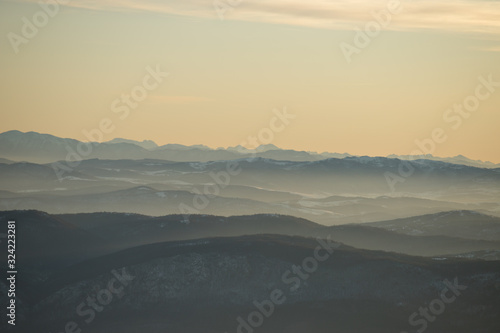 Beautiful view of the mountain range partially covered with snow just before sunset. Partly orange sunset sky © Zoran