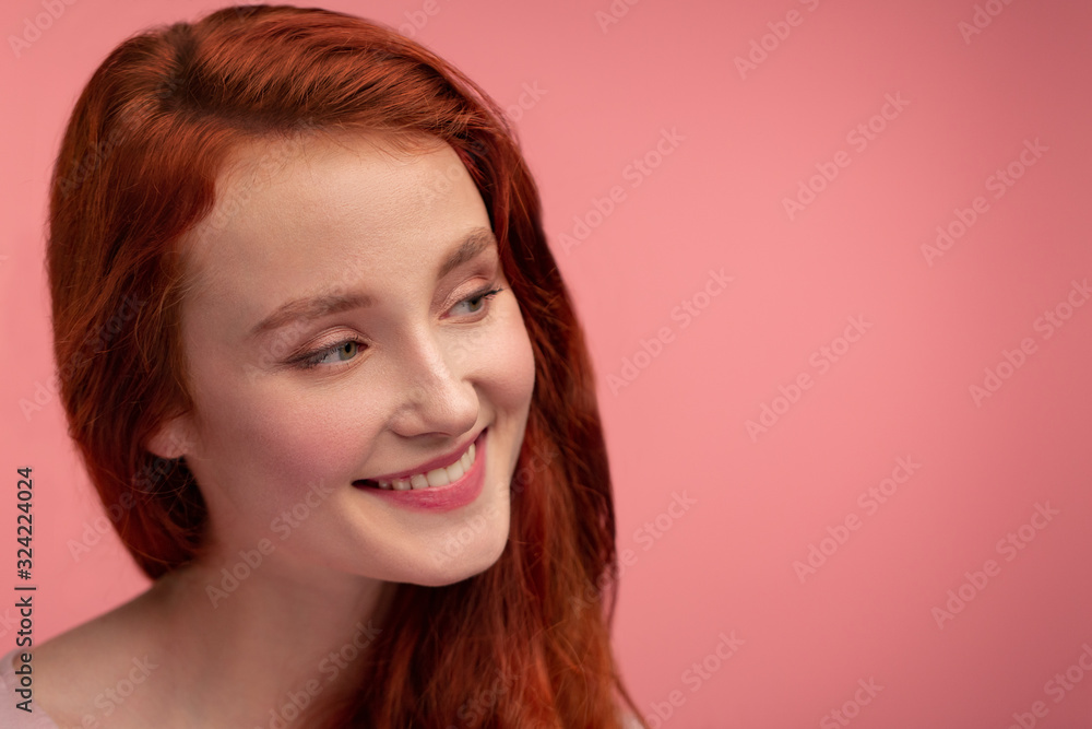 Portrait of smiling redhead girl. Perfect skin. Beautiful female model with long hair over pink background. Young cute woman with clear skin. Skincare and facial treatment concept. Portrait of smiling redhead girl. Perfect skin. Beautiful female model with long hair over pink background. Young cute woman with clear skin. Skincare and facial treatment concept.