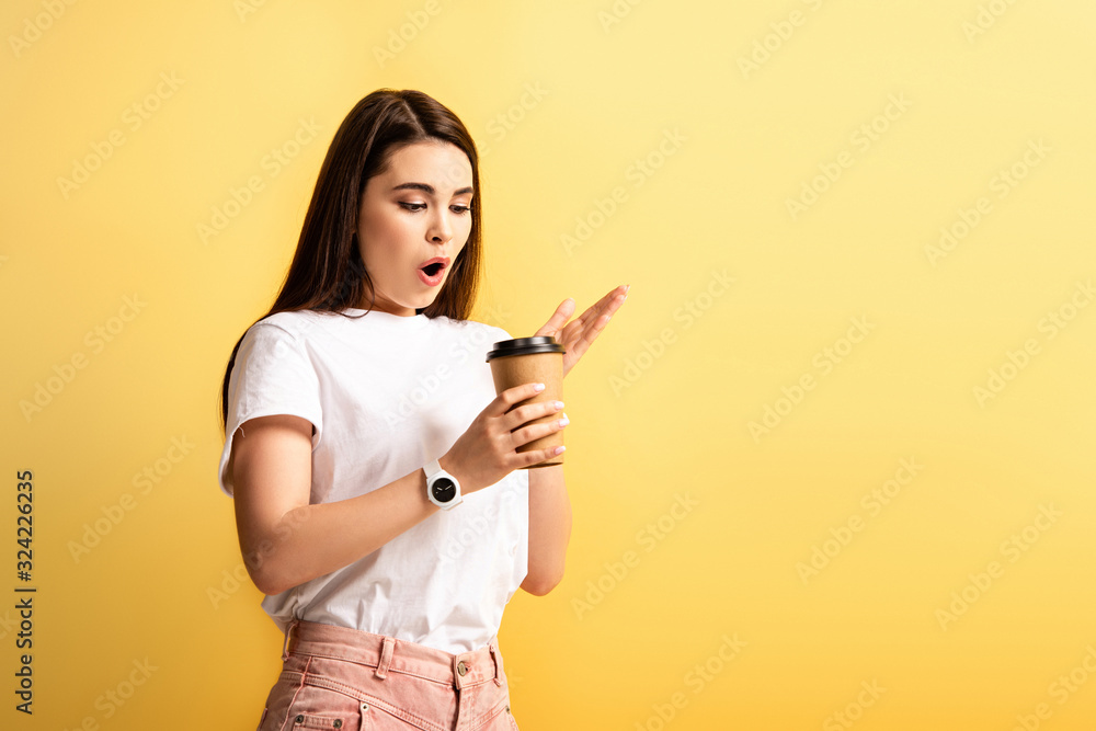 surprised girl standing with open mouth while holding coffee to go isolated on yellow surprised girl standing with open mouth while holding coffee to go isolated on yellow