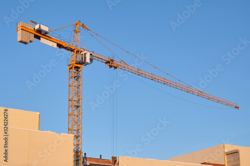 Yellow crane at a construction site against a clear blue sky. Crane and building working progress.