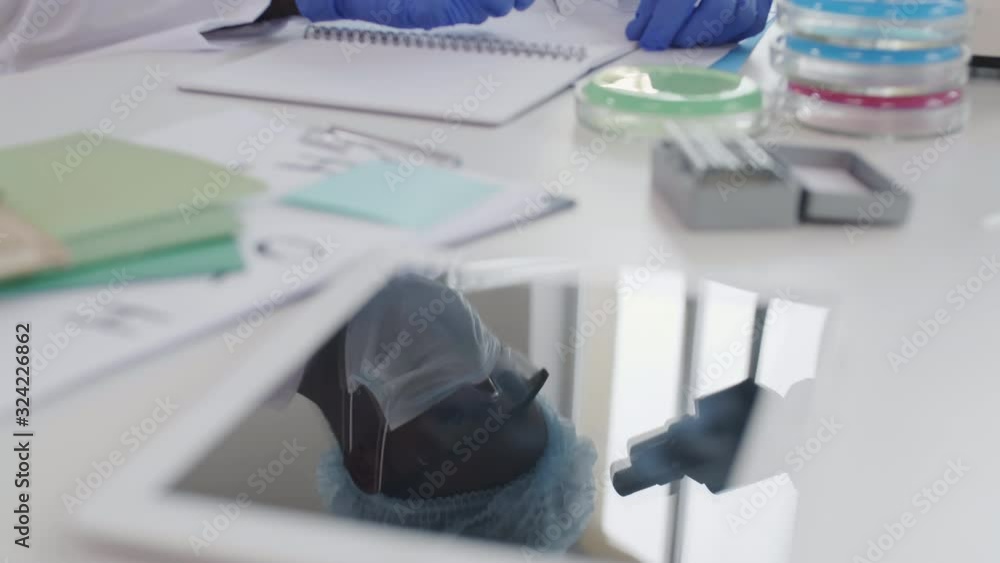 Close up of reflection of unrecognizable African scientist making research using microscope in lab Close up of reflection of unrecognizable African scientist making research using microscope in lab
