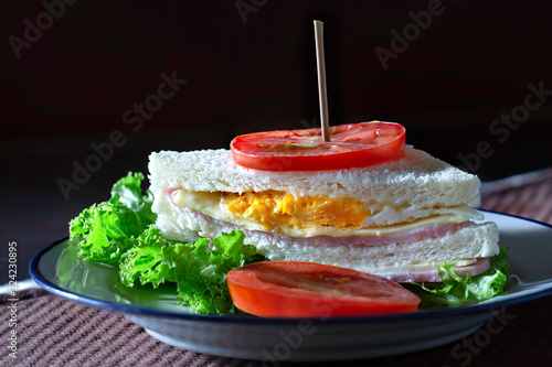 Sandwich cheese and ham and fried egg with veg. in white dish on dark brown apron and oranges juice in glass