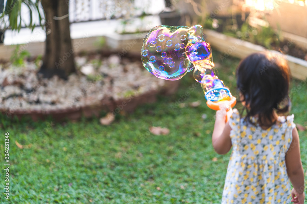 Cute little asian girl playing with soap bubbles in garden.