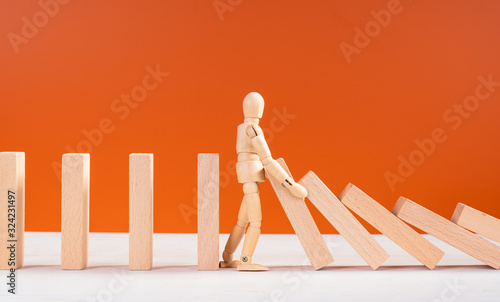 Wooden man stopping falling domino concept. Symbol of crisis, risk, management, leadership and determination. Domino effect. Fall of the crumbling business is saved by mannequin. Orange background.
