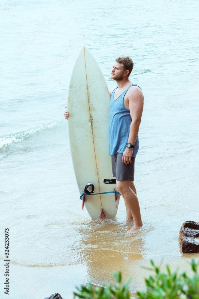 Naklejka premium Man with surfboard on the beach. Surfer in Sri Lanka Mirissa. Blue wave