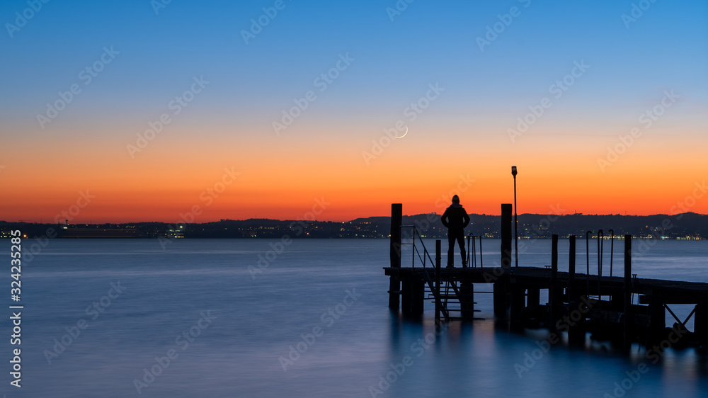 A man silhouette standing on wooden pier lonely at the sea with beautifulsunset. lsunset seascape at a wooden jetty A man silhouette standing on wooden pier lonely at the sea with beautifulsunset. lsunset seascape at a wooden jetty