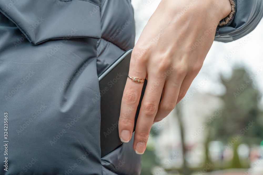woman's hand with a ring pulls a black smartphone out of the pocket of a gray jacket close up
