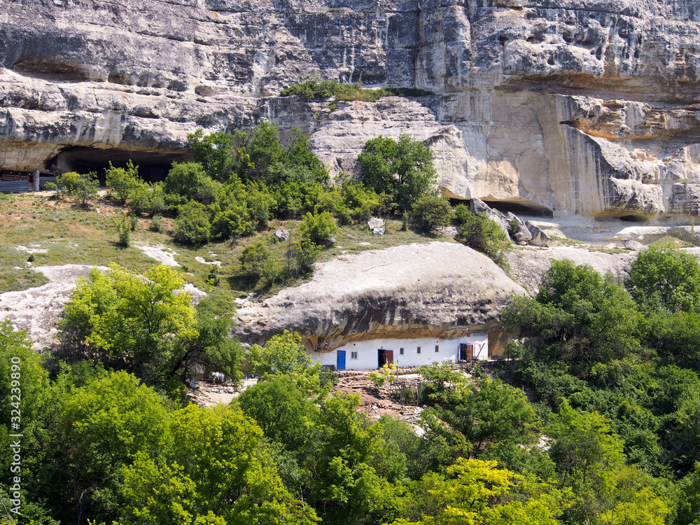 The house is built in a rock, white facade against a background of brown rocks and dense vegetation. Travel in the mountains, the concept of active recreation. The house is built in a rock, white facade against a background of brown rocks and dense vegetation. Travel in the mountains, the concept of active recreation.