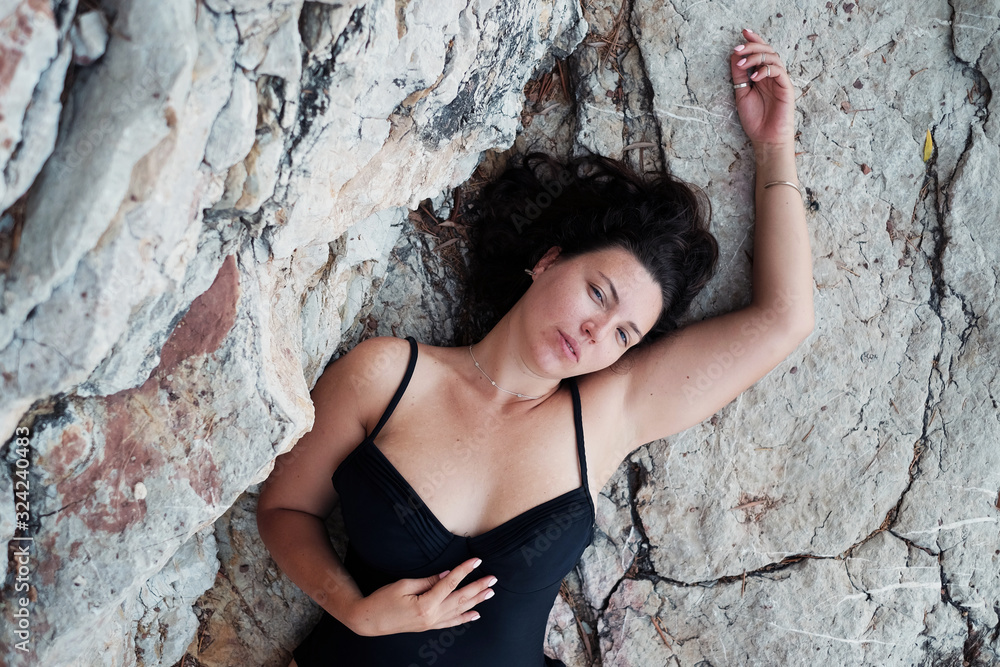 Top view model size plus in black swimming suit on the cliffs. Body Positive concept. Horizontal photo