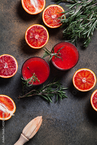 Fototapeta Naklejka Na Ścianę i Meble -  Blood orange juice with rosemary sprigs in a glass, sliced Sicilian blood oranges on a rustic background.