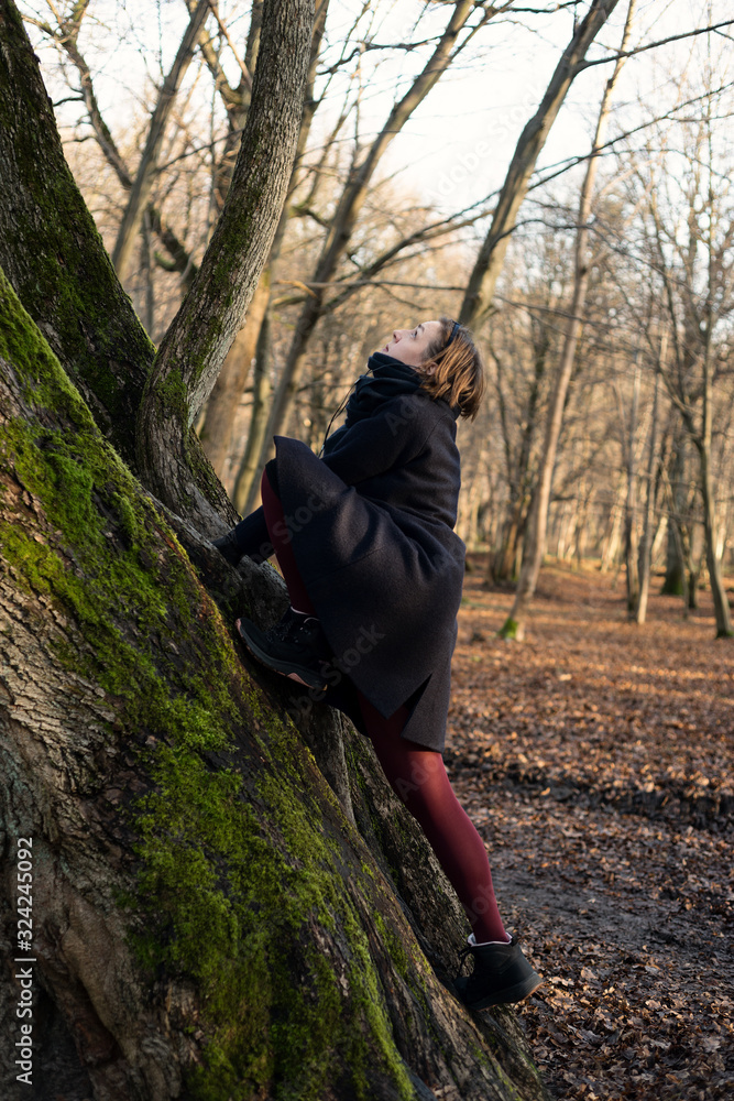 Woman climbs a tree in the park in headphones in autumn Woman climbs a tree in the park in headphones in autumn