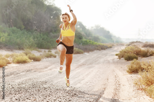 A young slender woman in sportswear runs on the sand against the background of trees on a Sunny day. Fitness, training, lifestyle
