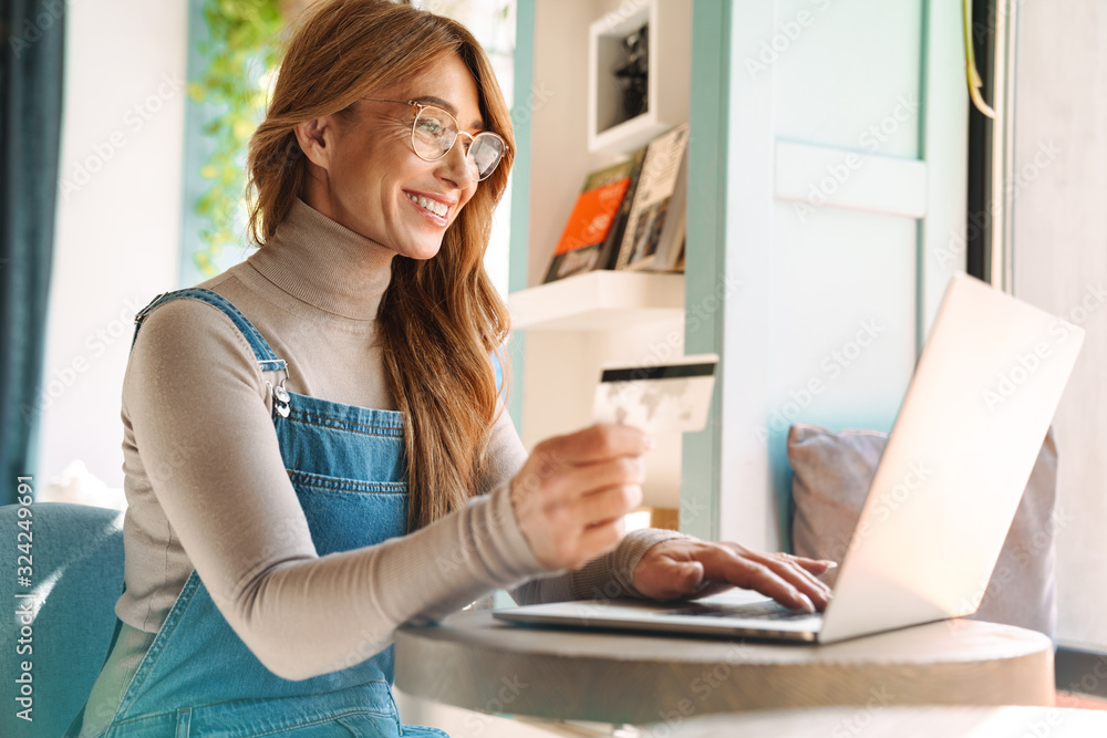 Photo of smiling mature woman holding credit card while using on laptop Photo of smiling mature woman holding credit card while using on laptop