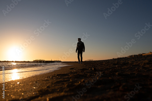 One man walking on the beach and looking at the sunset over the sea. Young man and sunset on Mediteranean sea. Solitary man. A colorful sunset sea, man observing the beauty of nature.
