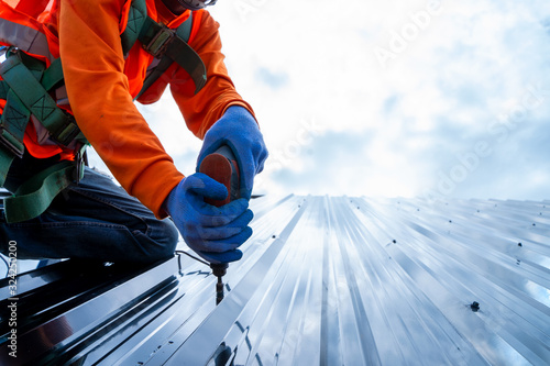 Canvas Print Close up photo of Professional and qualified roofer in protective uniform wear use electric drill to install the metal sheet on the new roof of new modern building construction