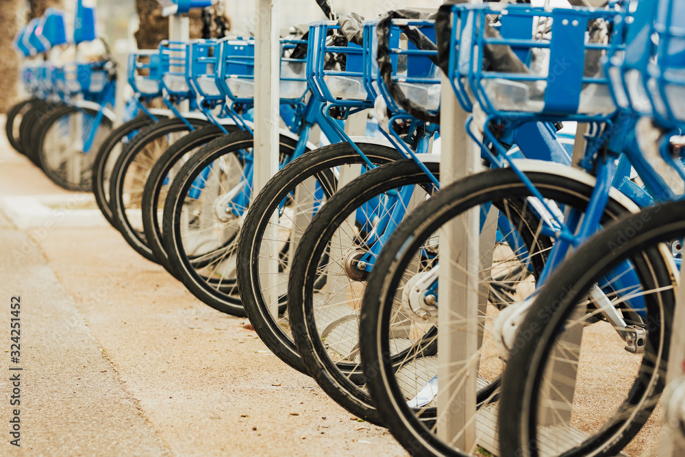 Bike sharing on the Promenade des Anglais. Rent of blue bikes at docking stations in city along a busy street in Nice, France. Velo Rental. Hire Bike Station. Bike sharing on the Promenade des Anglais. Rent of blue bikes at docking stations in city along a busy street in Nice, France. Velo Rental. Hire Bike Station.
