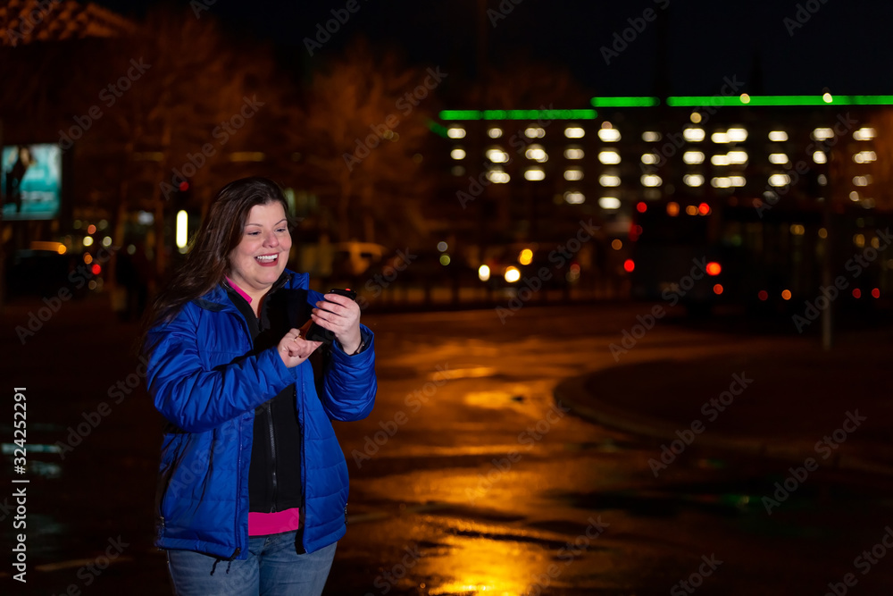 Fototapeta premium Lady chats via sms with her smartphone when she is outside in the city at night.