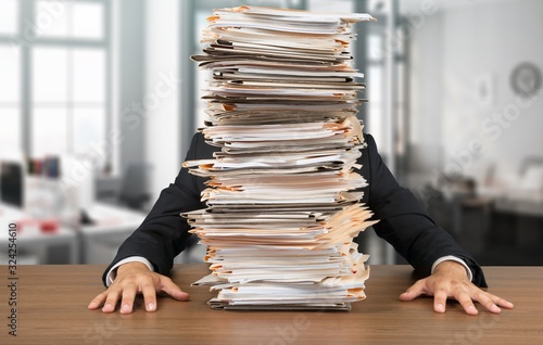 Young businessman hid behind with stack of papers on wooden table