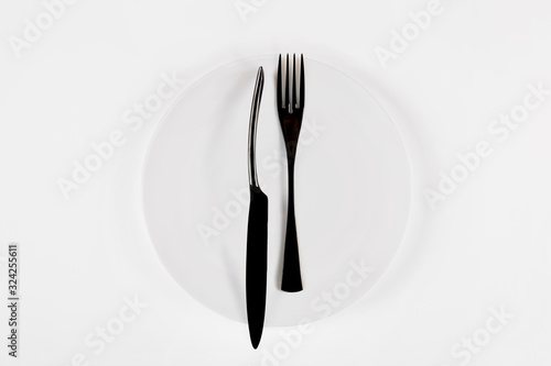 White ceramic round plate with black cutlery isolated on white.