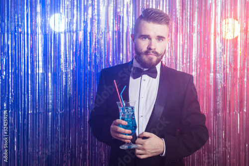 Sticker Club party and holidays concept - Portrait of elegant handsome man in a expensive suit drinks blue cocktail on shiny background