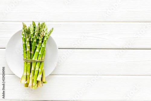 Asparagus. Banch of fresh steams on plate on white wooden background top-down copy space