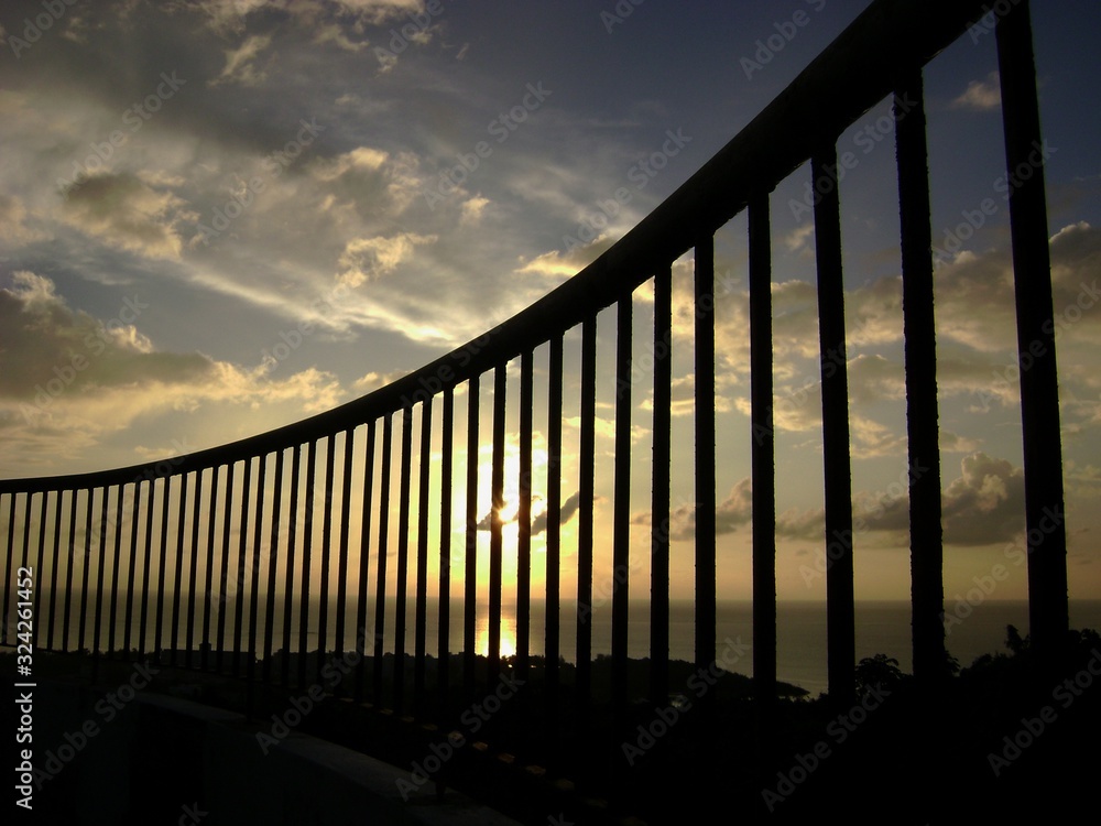 Sunset seen through the bars of a steel railing by the beach