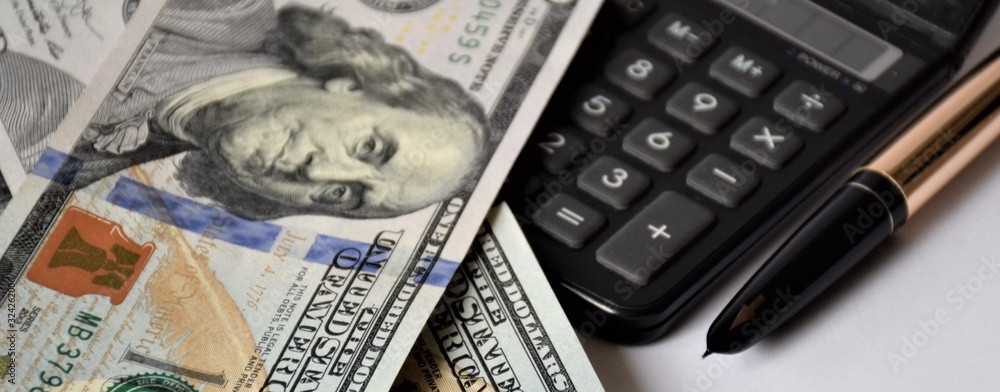a pile of dollars banknotes on a white background, with a golden pen, calculator, business concept a pile of dollars banknotes on a white background, with a golden pen, calculator, business concept