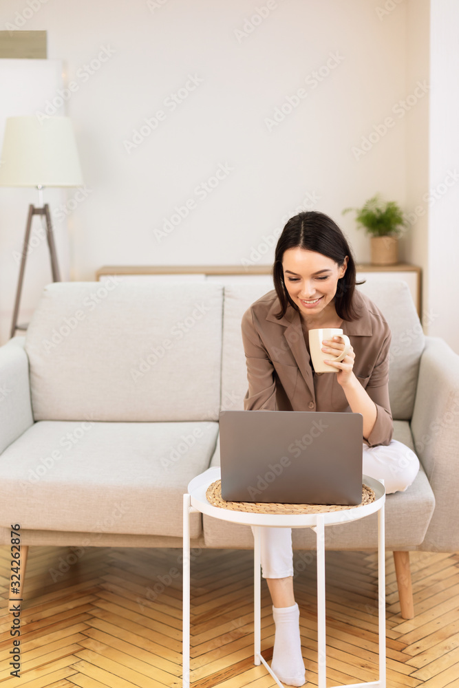 Young woman using laptop sitting on the couch with tea Young woman using laptop sitting on the couch with tea